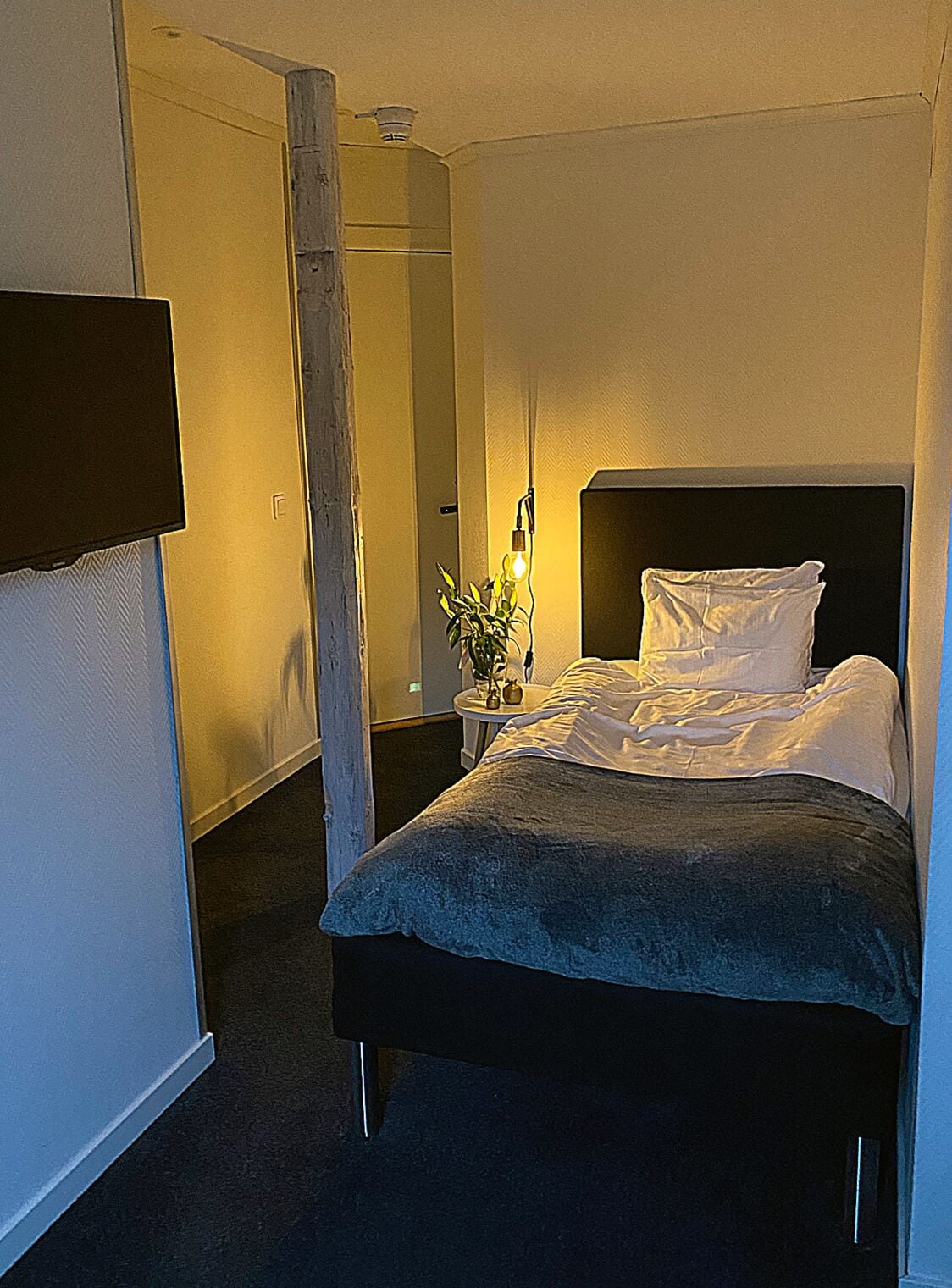 Ein Schlafzimmer mit einem Bett, einem Nachttisch und einem an der Wand befestigten Fernseher.