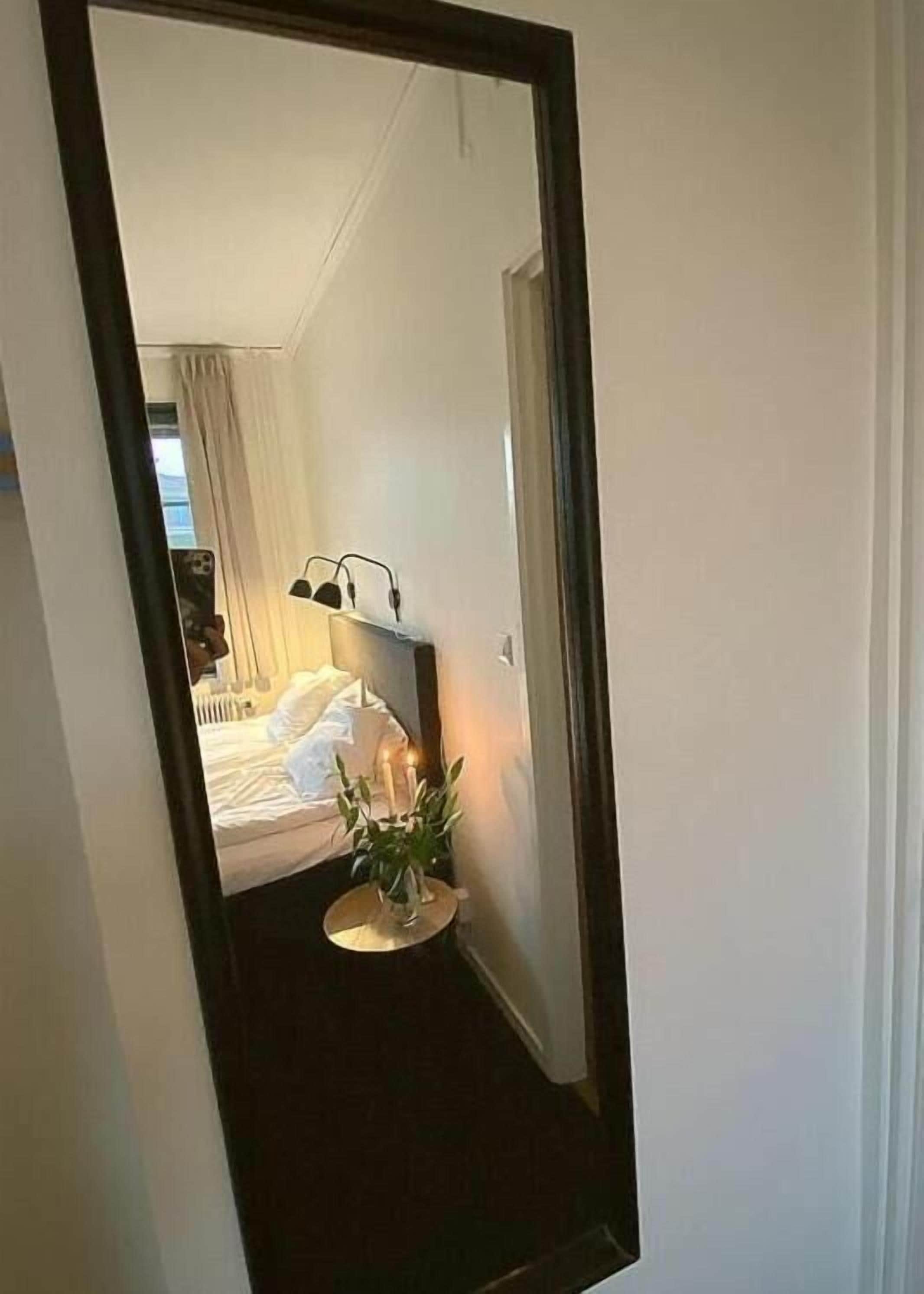 Een slaapkamer met een bed, nachtkastje en een spiegel die de kamer weerspiegelt.
