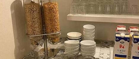 Una barra de desayuno con dispensadores de cereales, platos apilados y cartones de leche.