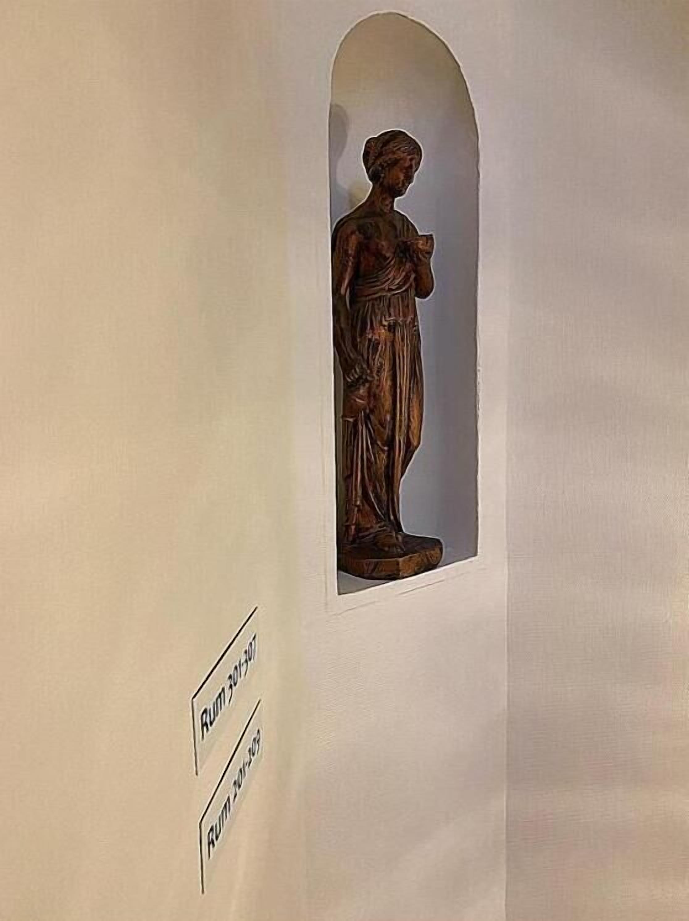 A wooden statue of a woman in a niche with inscriptions.