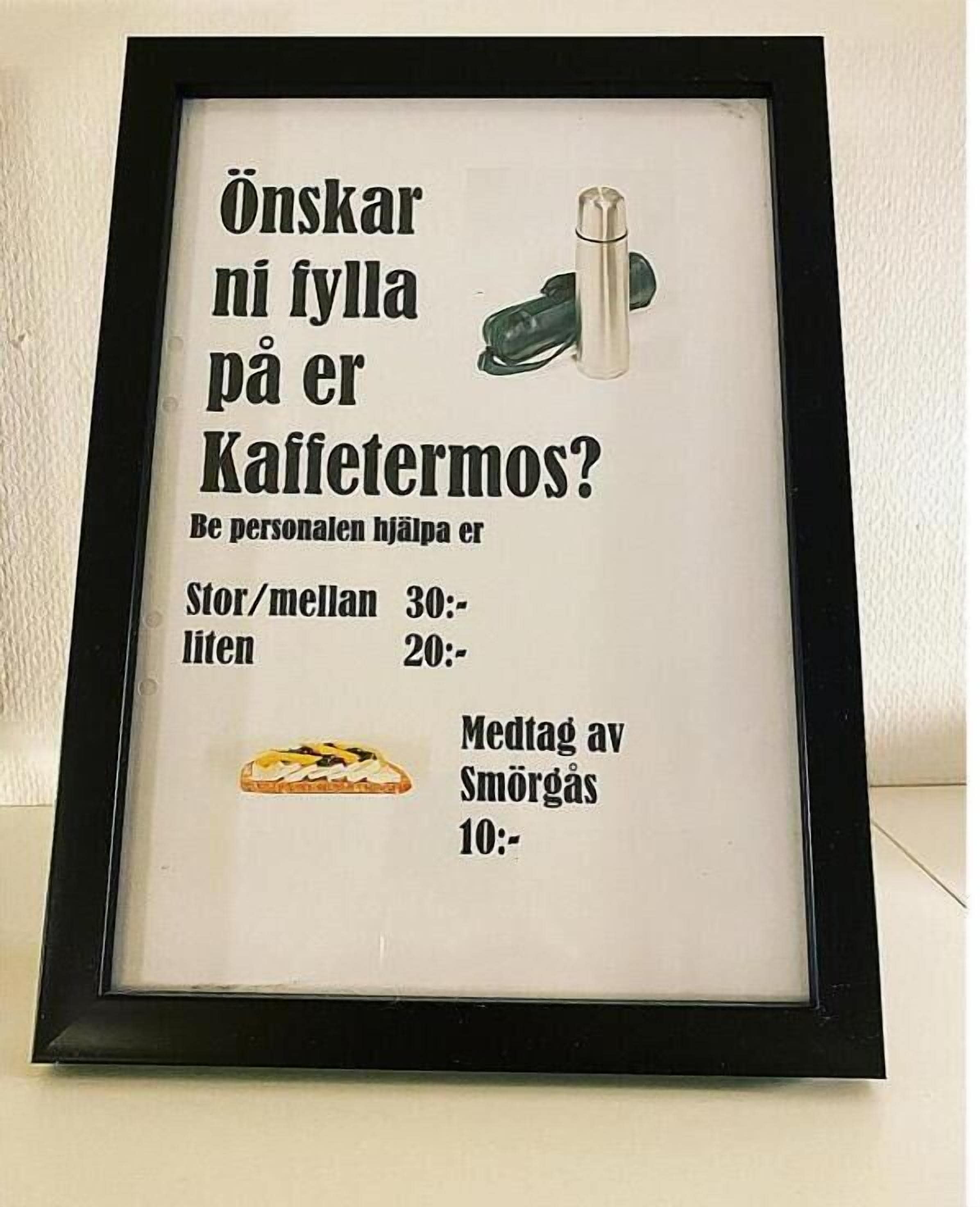 Un cartell amb marc, amb text en suec, que indica l'hora per a una pausa cafè i l'hora per a dinar.