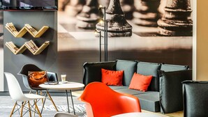 A modern lounge area with a sofa, chairs, a coffee table, and a television mounted on the wall. - ibis Hotel Köln Messe (Cologne)