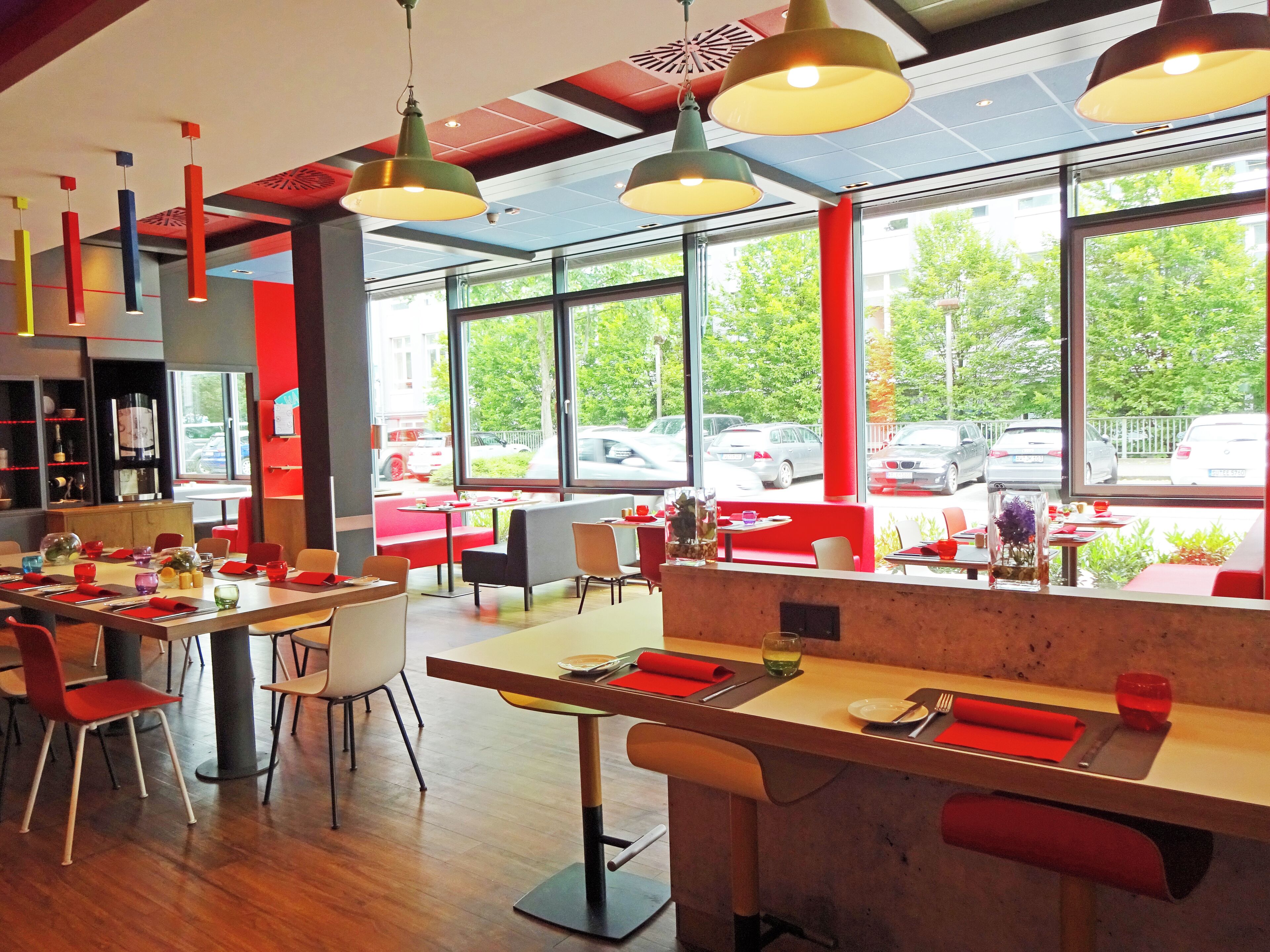 Un interno ristorante moderno con soffitti alti, ampie finestre e dettagli rossi.