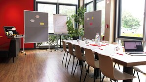 Une salle de conférence équipée d’une longue table, de chaises, d’un ordinateur portable, d’un tableau blanc et d’un écran de présentation.
