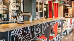 A bar area with a wooden counter, modern pendant lights, and red chairs. - ibis Hotel Köln Messe (Cologne)