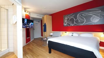 Ein Hotelzimmer mit einem großen Bett, einem Fernseher, einer roten Akzentwand und einem Holzboden.