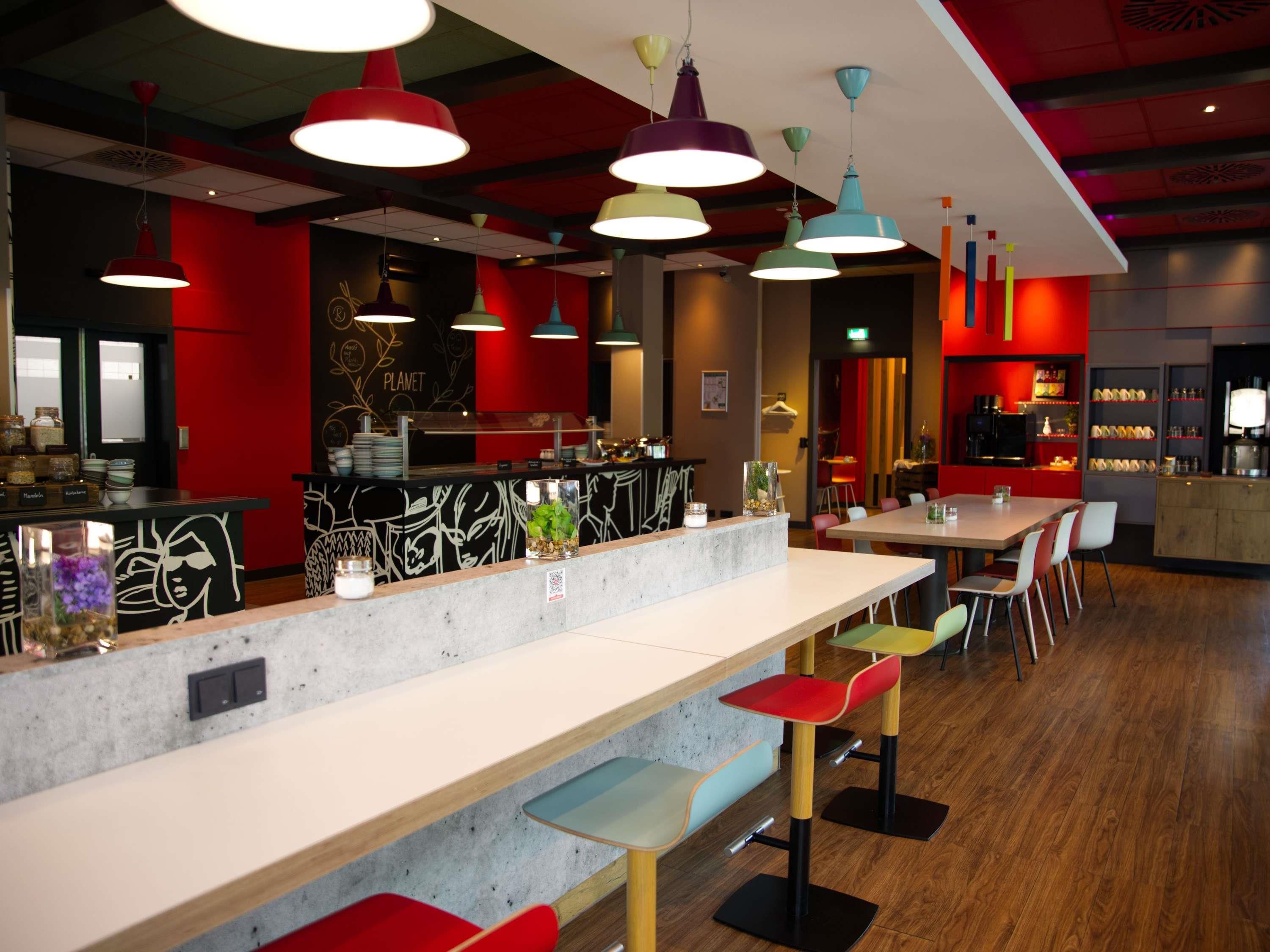Un interior de cafetería moderna con una barra larga, diversas opciones de asientos e iluminación colgante de colores.