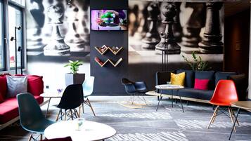 Ein stilvoller Lounge-Bereich mit Wandbild einer Schachfigur, bequemen Sitzgelegenheiten und einem Fernsehbildschirm.