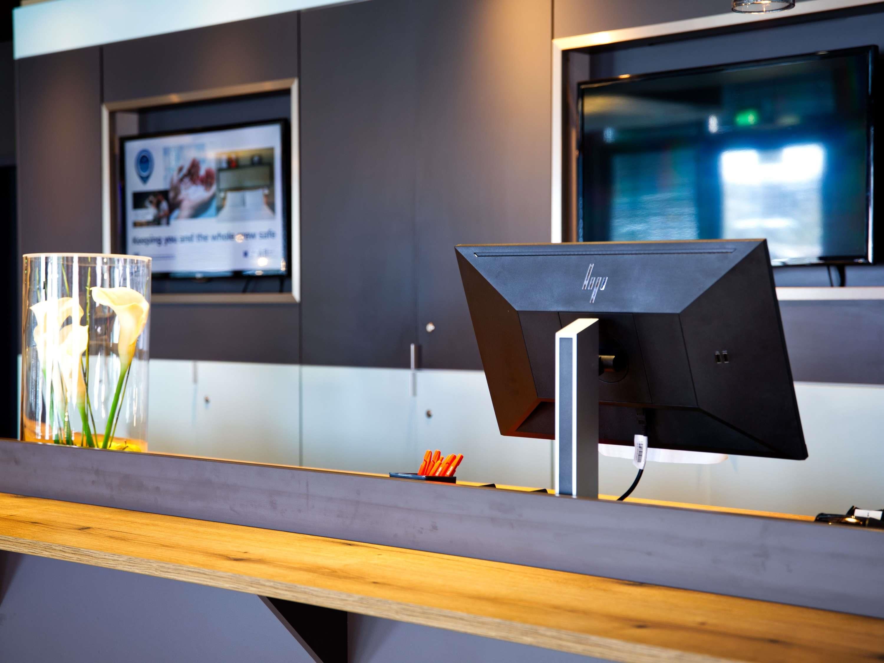 A reception desk with a modern design, a glass vase with flowers, and a framed poster on the wall.
