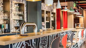 A bar area with a wooden counter, modern pendant lights, and red chairs.