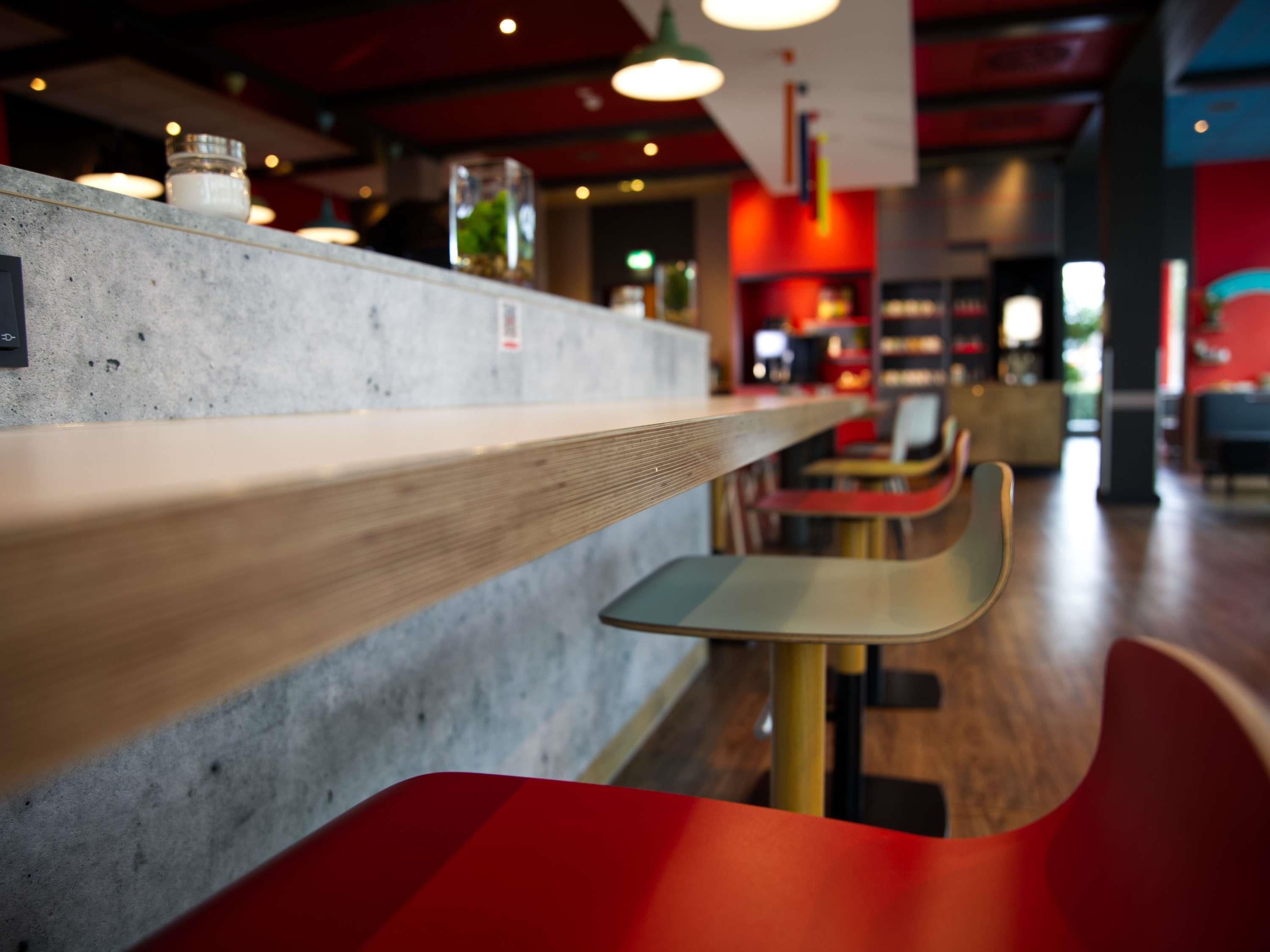Zona de bar con mostrador de hormigón, estanterías de madera y asientos rojos.