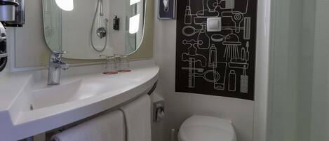 A bathroom with a white sink, mirror, and toilet. There is a towel rack and a showerhead.