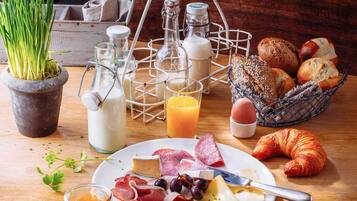 A breakfast setting with a plate of cheese, meats, and olives, a croissant, and a basket of bread.