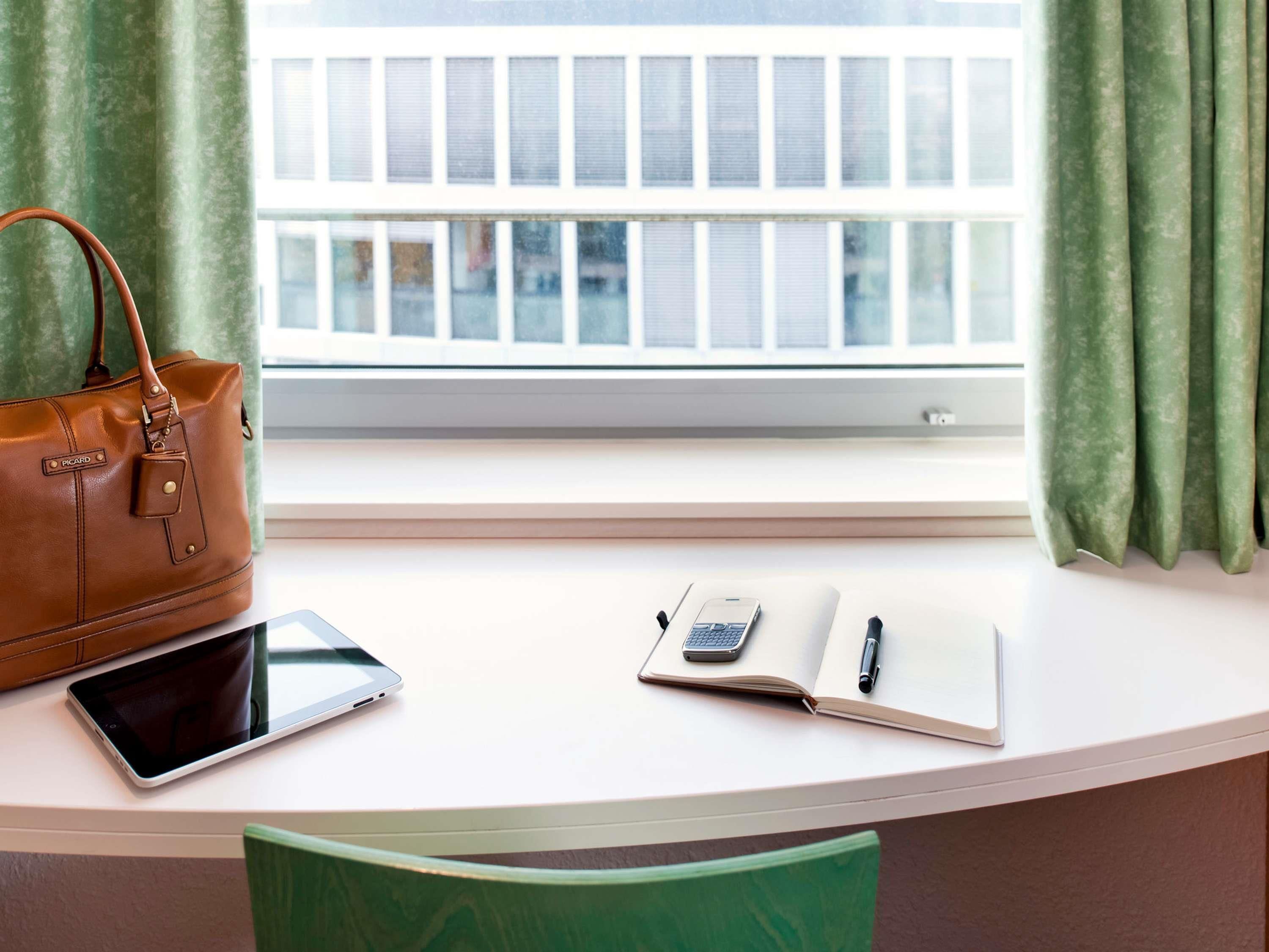 A desk with a laptop, a smartphone, a notebook, and a pen. A brown handbag is placed on the left side of the desk.