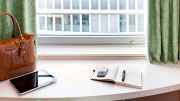 Een bureau met een laptop, een smartphone, een notitieboekje en een pen. Een bruine handtas ligt aan de linkerzijde van het bureau.