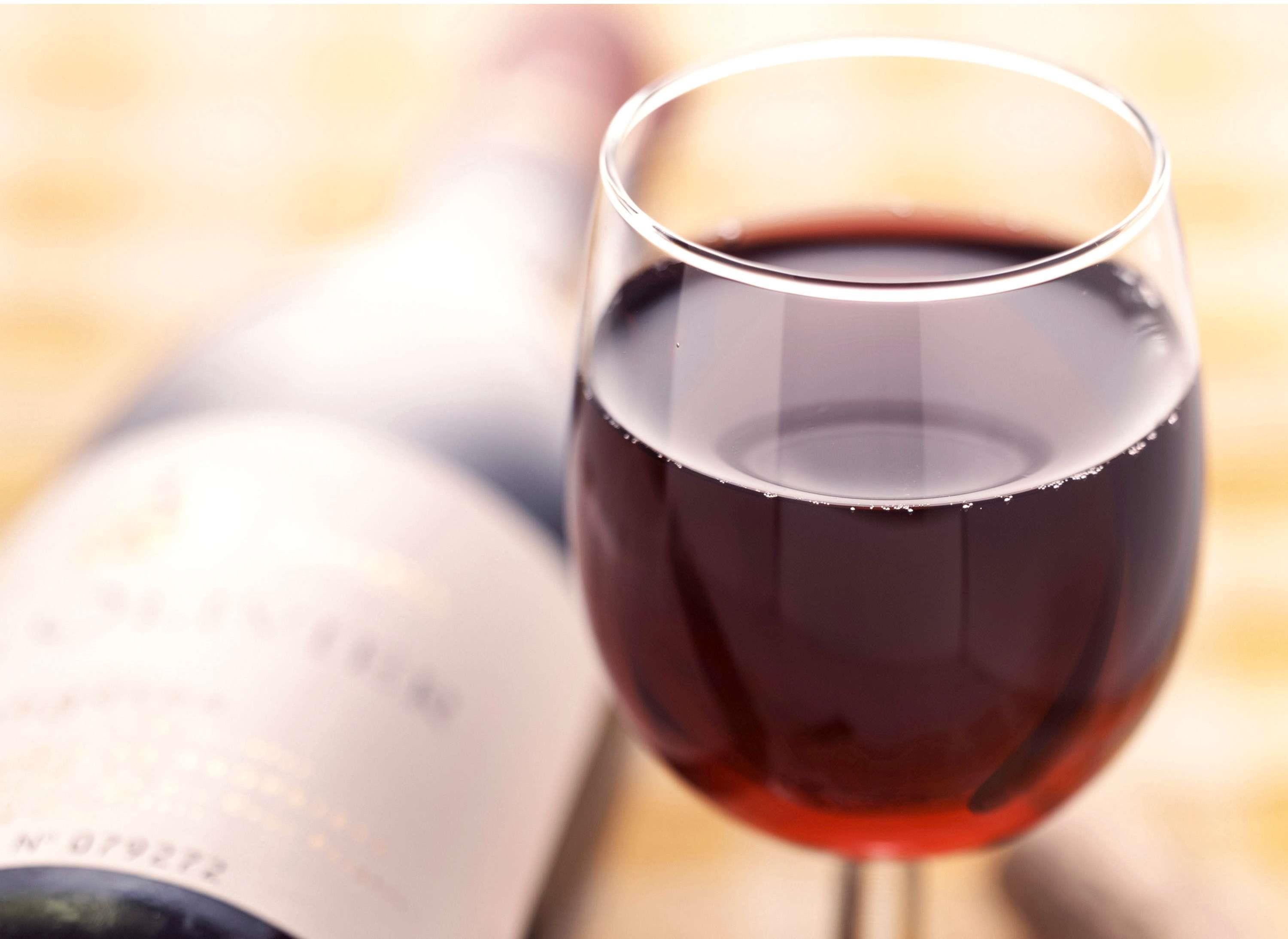 A wine glass filled with red wine, a blurred bottle in the background, and a soft-focus background.