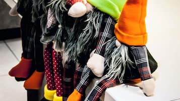 Una hilera de gnomos de jardín con sombreros de colores sobre un repisa.
