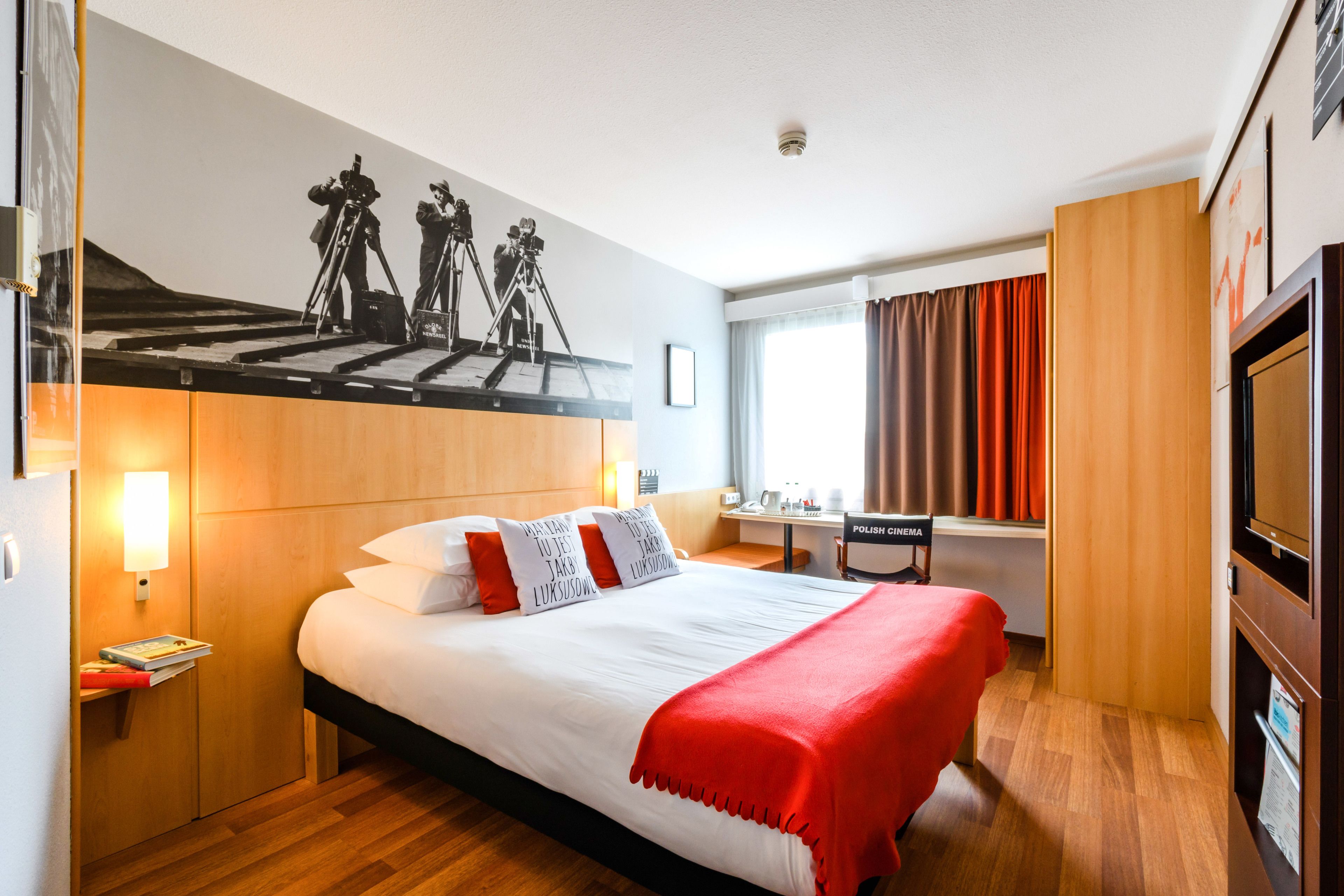 Habitación de hotel con una cama grande, un escritorio, televisión y un cuadro colgado en la pared de un fotógrafo.