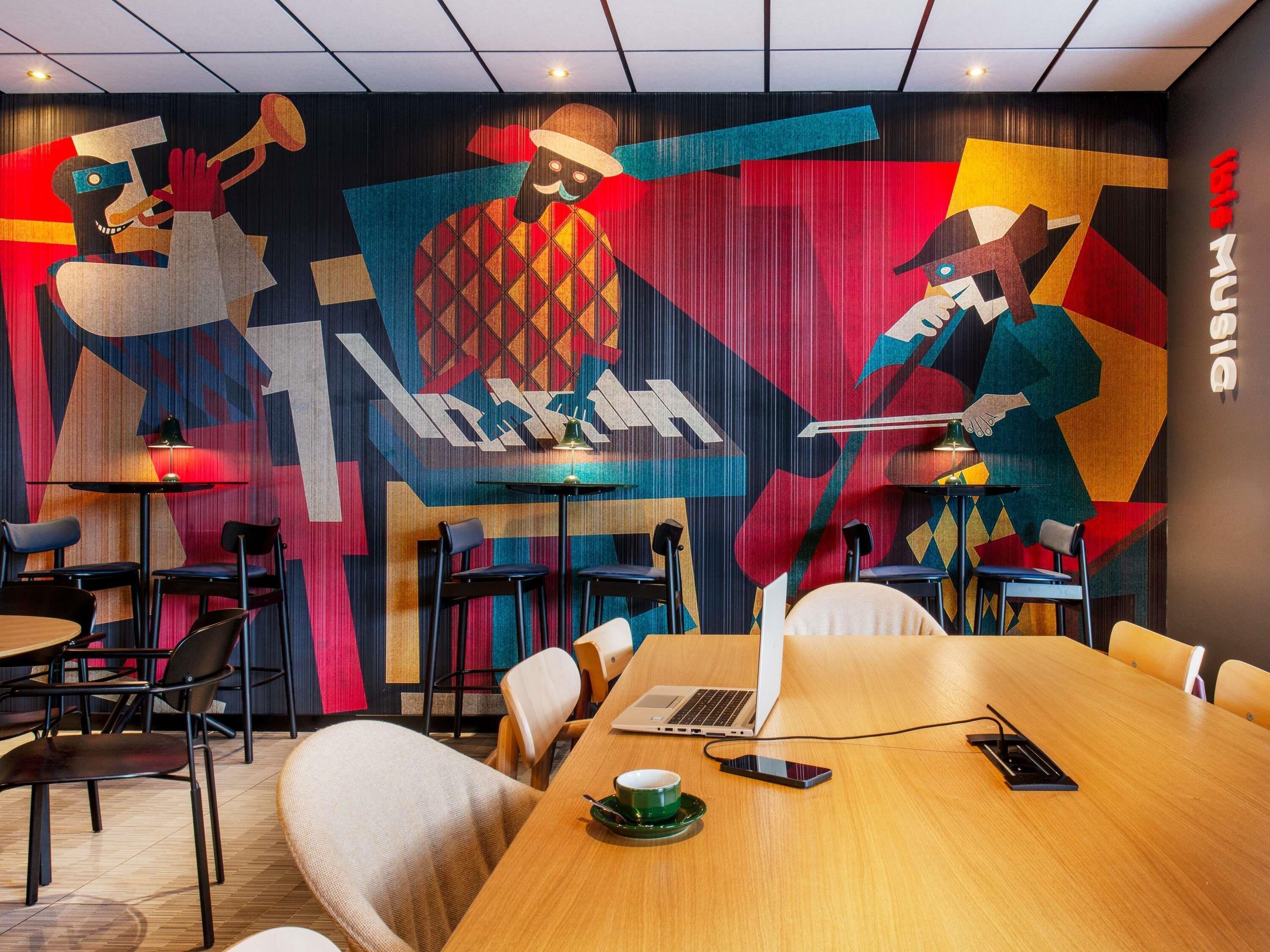 A modern conference room with a vibrant abstract mural, a wooden table with a laptop, and a cup of coffee.