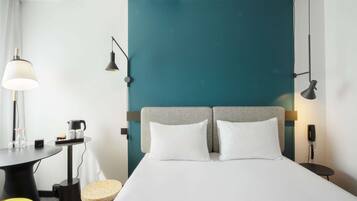 Habitación de hotel con cama, dos lámparas de noche, escritorio con lámpara, una silla y una mesita redonda.
