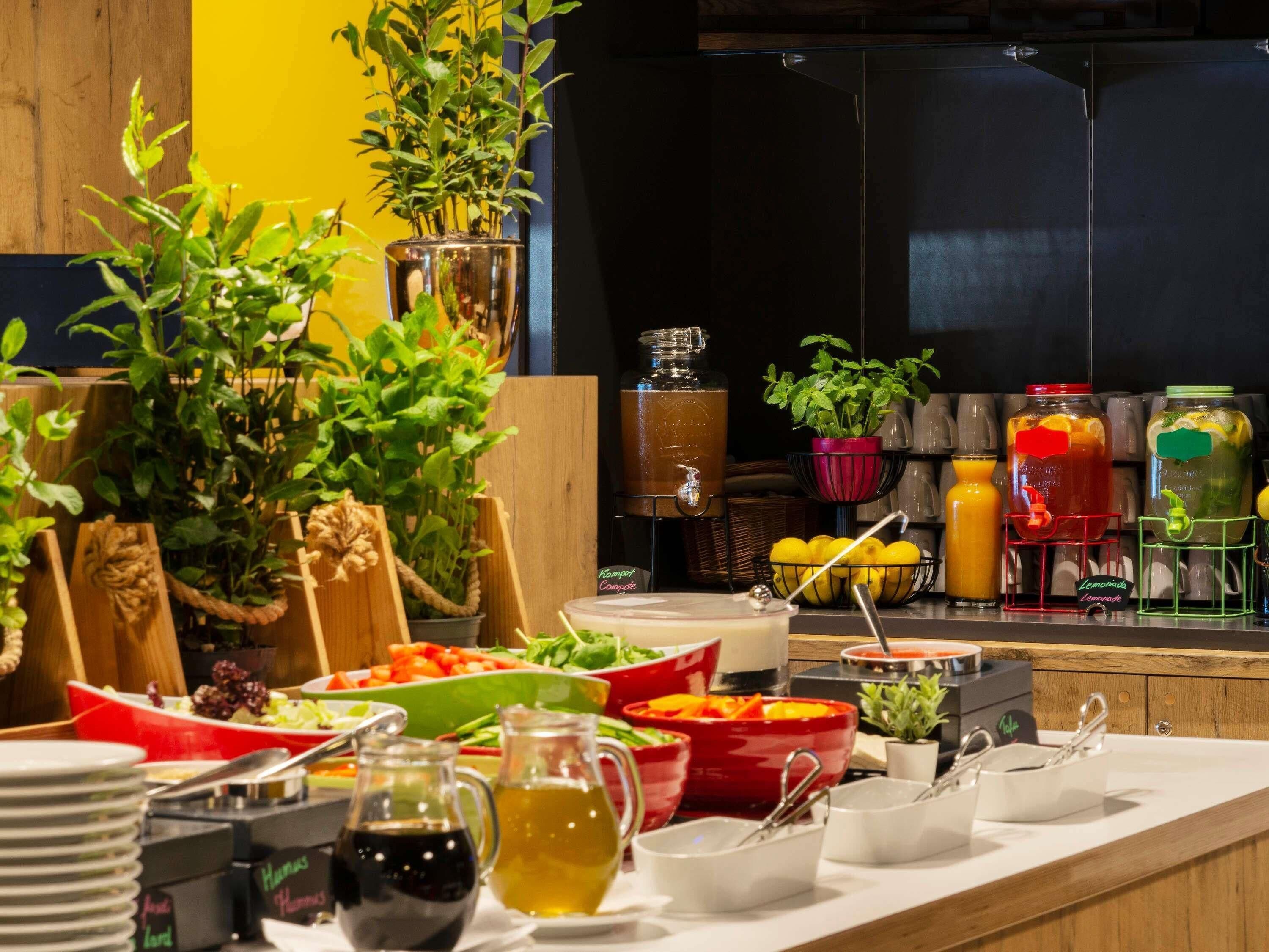 A buffet setup with various food items, drinks, and decorative plants.