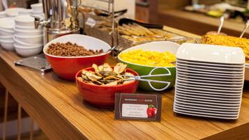 Un bufé con diversos alimentos, incluyendo tazones de cereales, frutas y un letrero que indica los sabores disponibles.