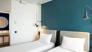 Une chambre d’hôtel moderne avec deux lits, une salle de bain et un mur d’accent de couleur turquoise.