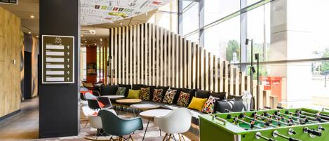 A modern lobby with a foosball table, seating area, and a wall with directional signs.