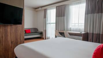 Una habitación de hotel con cama, escritorio, televisor, sofá y cortinas.
