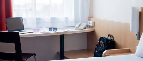 Habitación de hotel con escritorio, computadora portátil, gafas, teléfono y bolso.