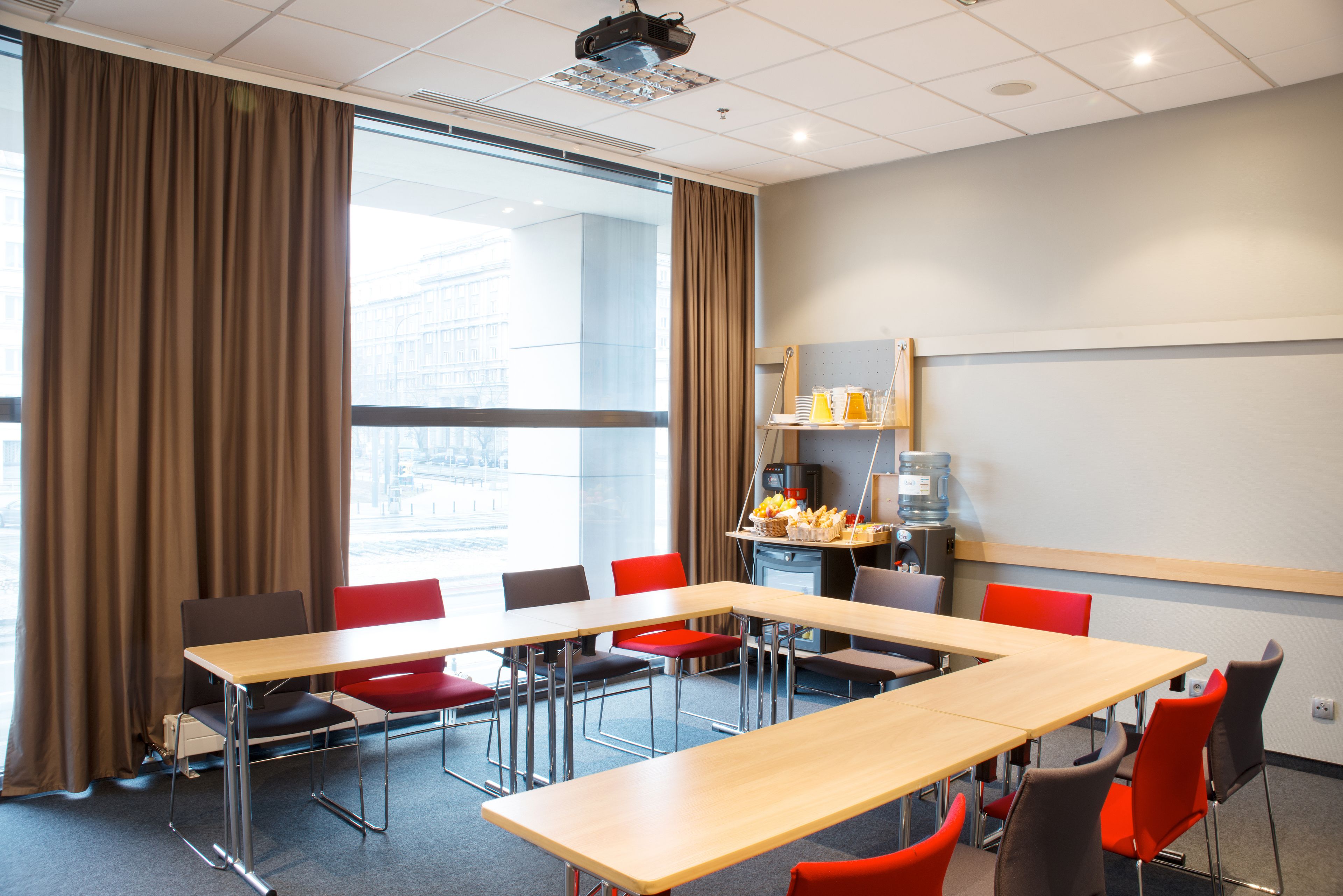 A conference room with a large table, red and black chairs, a projector, and a whiteboard.