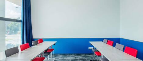 A conference room with a long table, red and gray chairs, a blue accent wall, and a large window.
