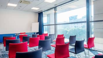 A conference room with rows of red and black chairs, a whiteboard, and a projector on the ceiling.