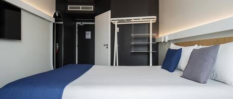 Una habitación de hotel moderna con una cama grande, un televisor de pantalla plana montado en la pared y un diseño de techo con una lámpara original.