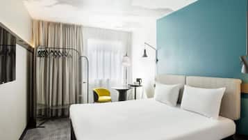 A hotel room with a bed, a desk, a chair, a wardrobe, and a window with curtains.