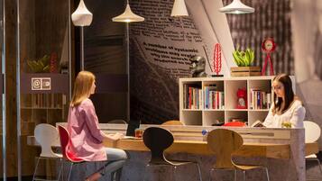 A modern bar area with a bar counter, stools, hanging pendant lights, and a bookshelf with books.