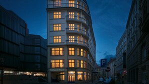 A multi-story hotel with a curved facade, illuminated windows, and a visible entrance with a sign. - Hotel Astoria (Prague)