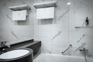 Un bagno moderno con rivestimento in marmo, una vasca da bagno dotata di doccetta, un mobile lavabo e due asciugamani su un portasciugamani.