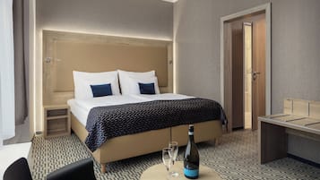 Habitación de hotel con una cama grande, mesitas de noche, un escritorio y una silla. Hay una botella de champán y dos copas en el suelo.