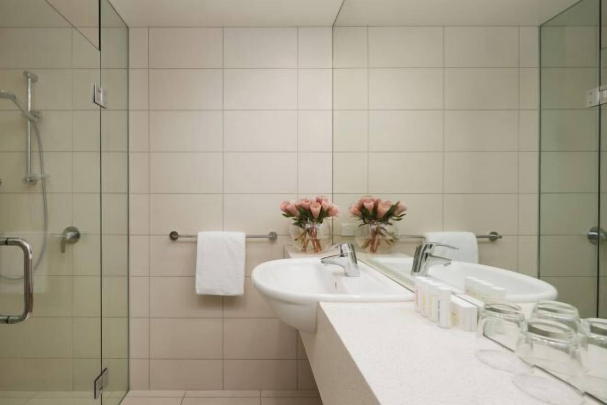 Un baño moderno con cabina de ducha de vidrio, dos lavamanos y un mueble de tocador con artículos de aseo.