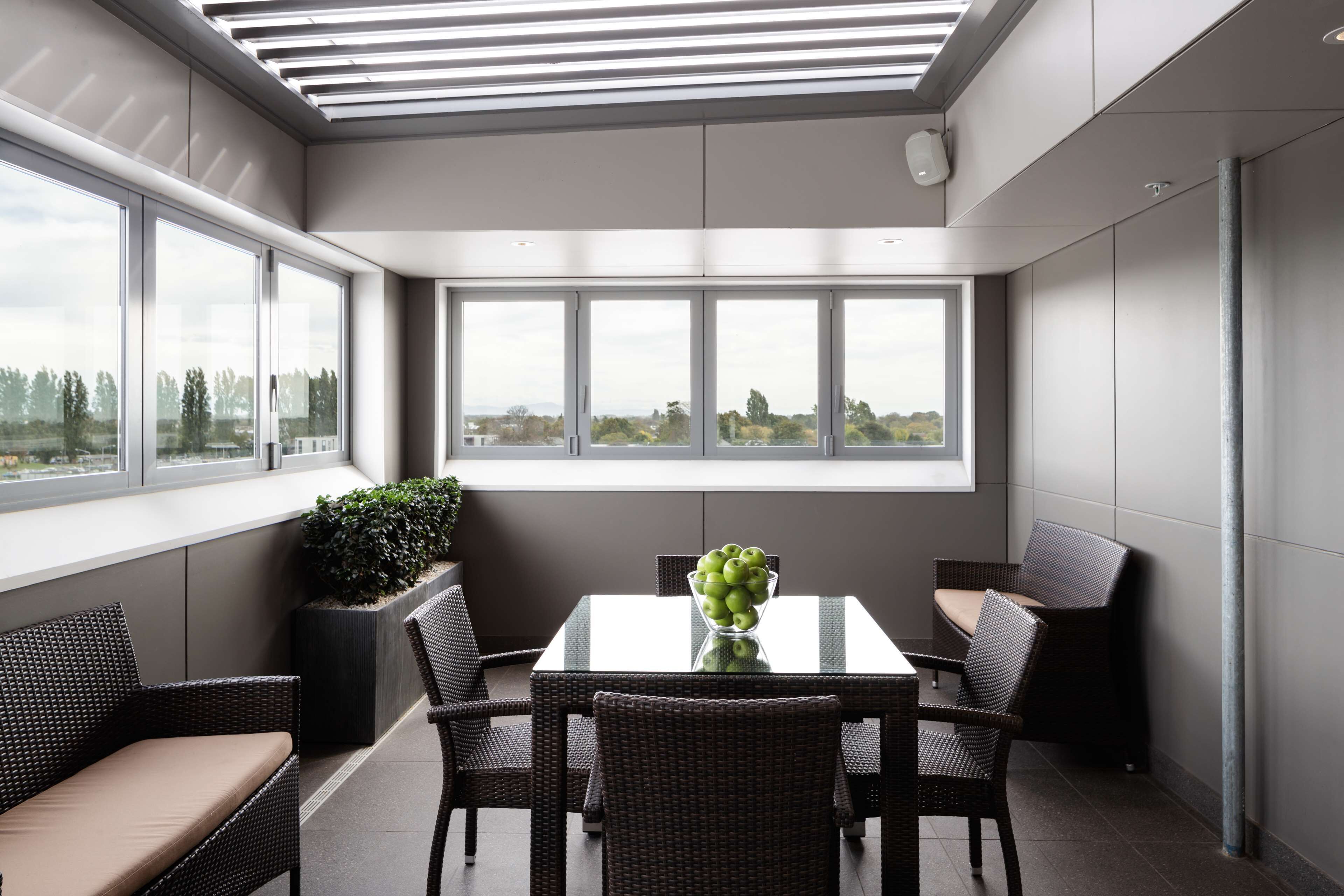 Un'area pranzo moderna con un tavolo in vetro, sedie in vimini e una vista attraverso ampie finestre.