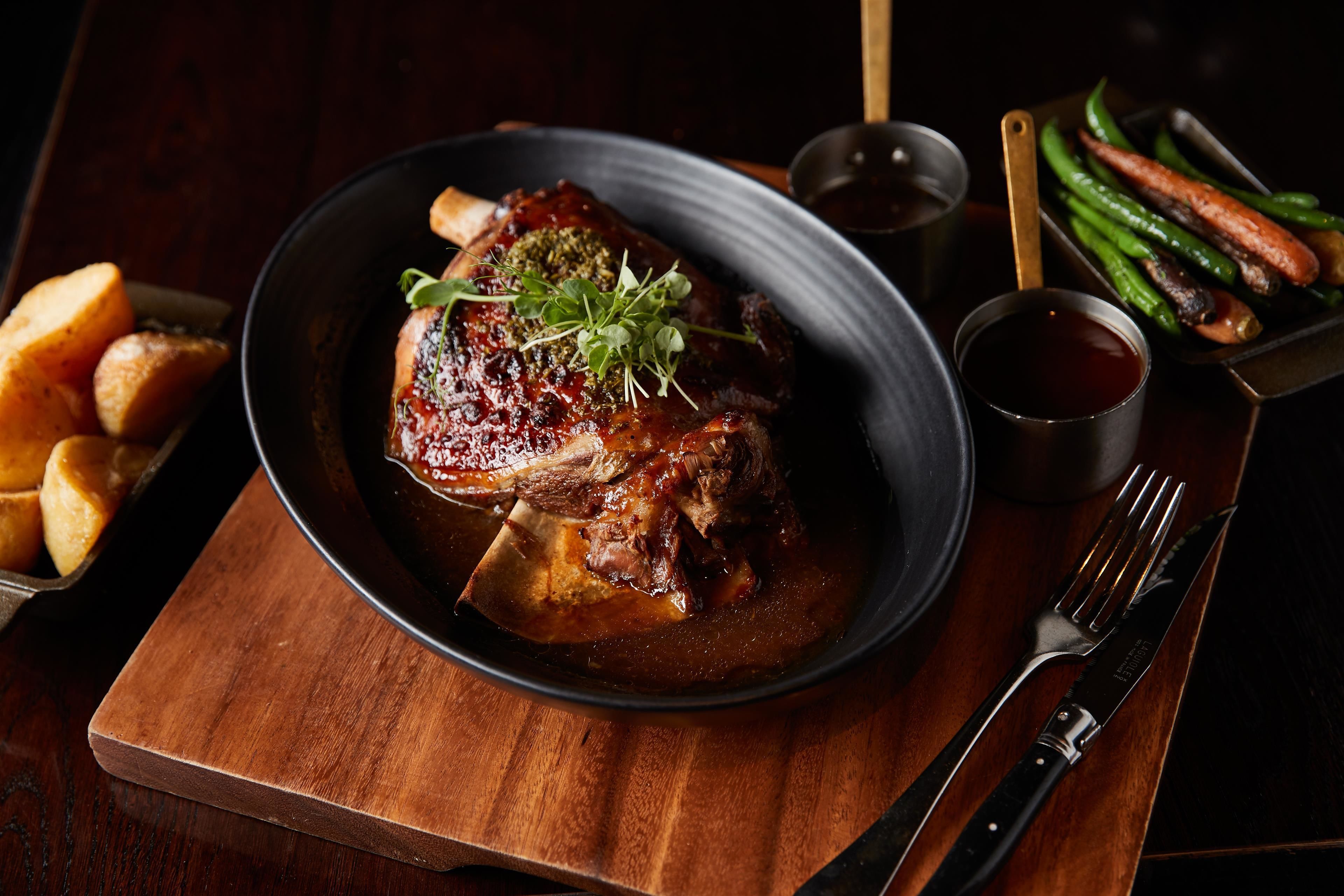 A plate of braised meat with vegetables and a small bowl of sauce.