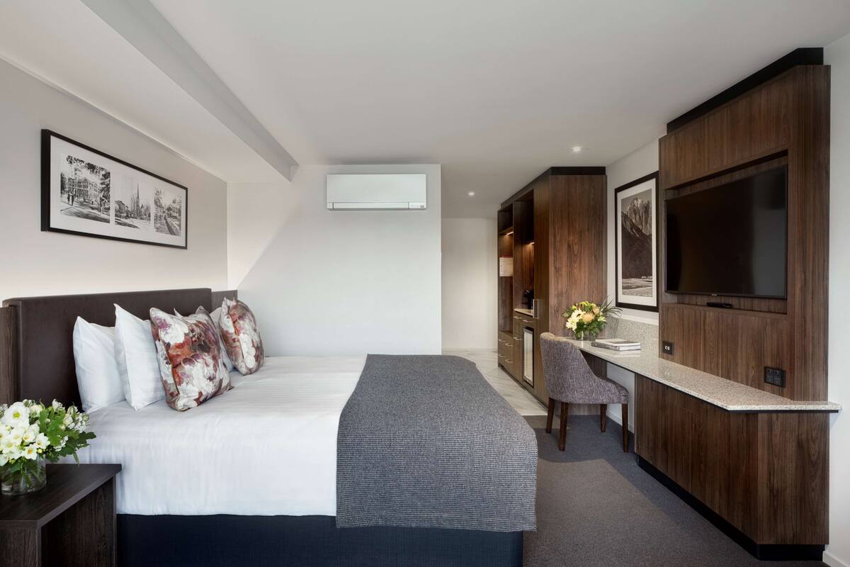 Una habitación de hotel moderna con una cama grande, un escritorio, un televisor y un cuadro enmarcado en la pared.