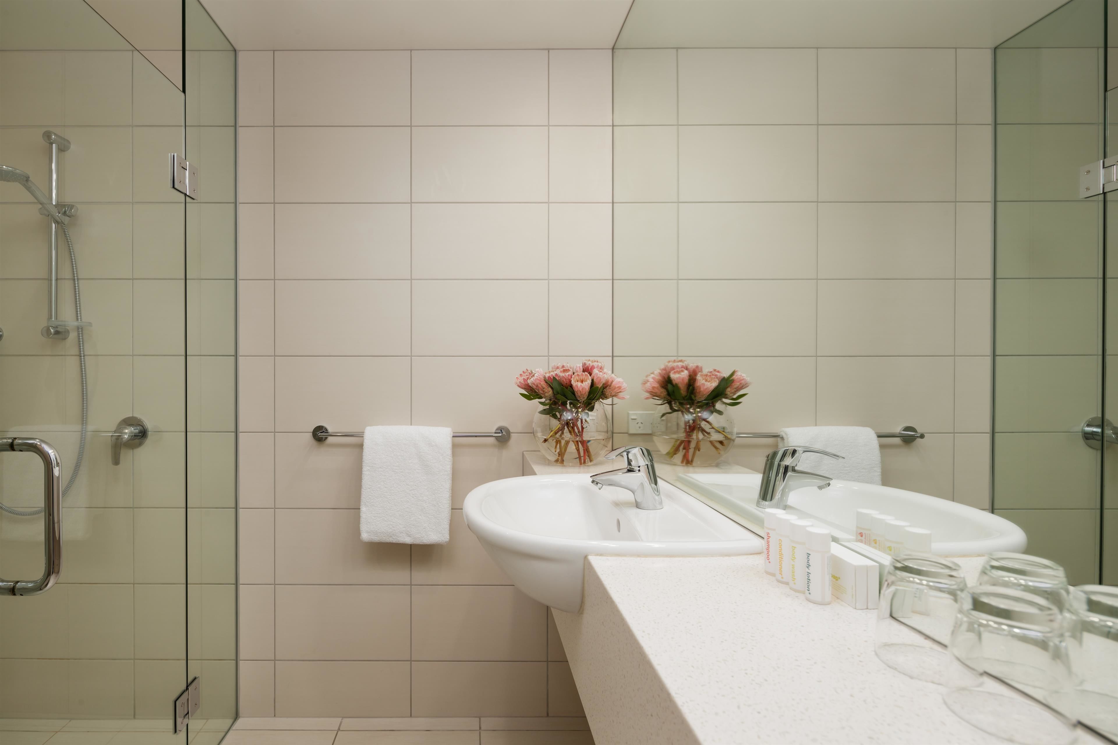 A modern bathroom with a glass shower enclosure, a white sink, and a vanity with toiletries.