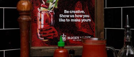 A kitchen counter with a recipe poster, a pepper mill, a bottle of hot sauce, a pitcher, and a bowl of lemons and celery.