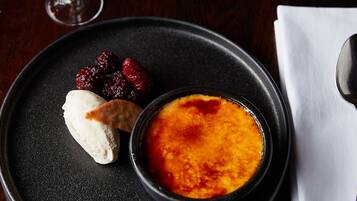 A dessert plate with a crème brûlée, berries, and a scoop of ice cream, accompanied by a glass of wine on a dark table.