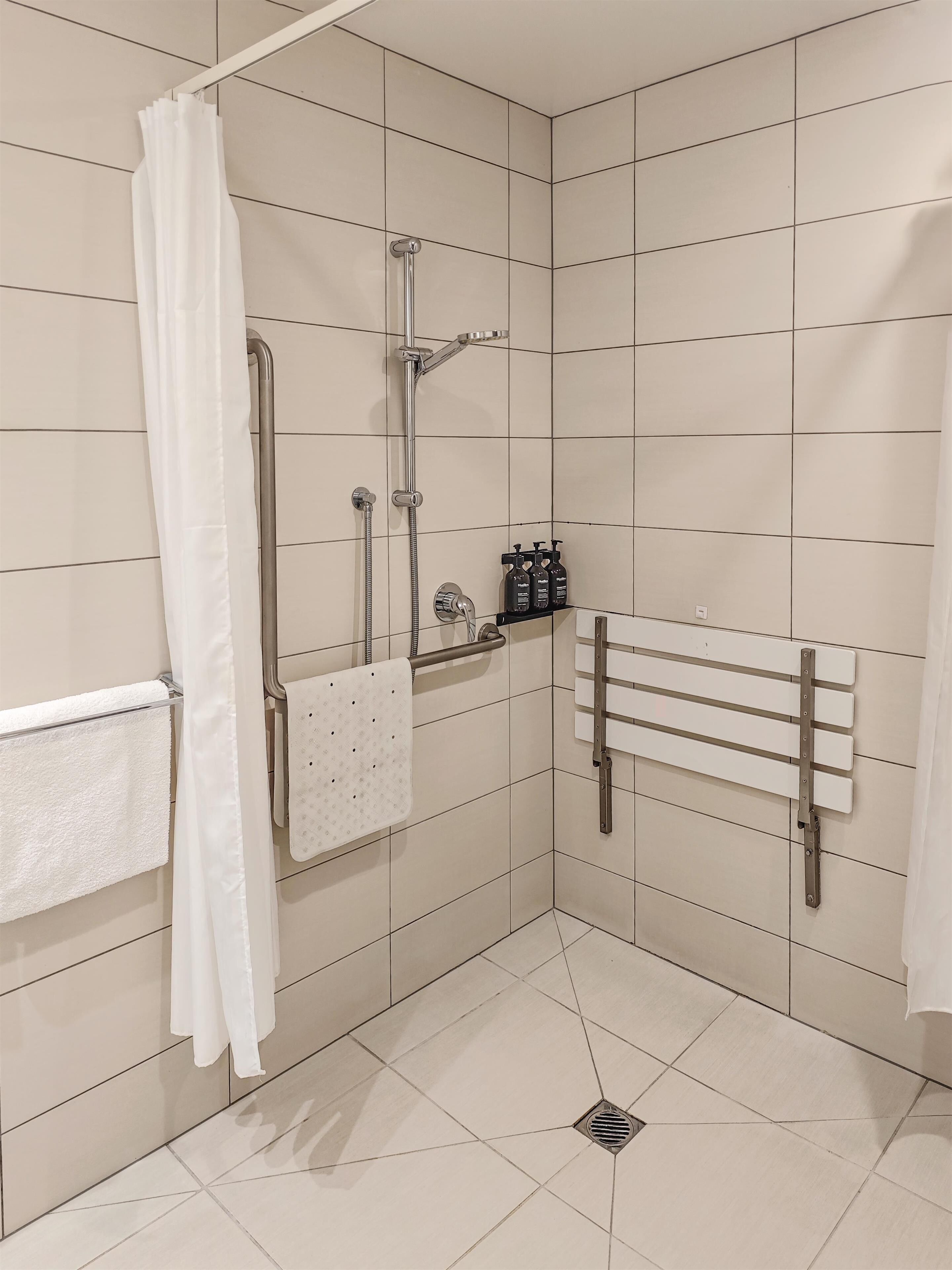 A modern shower area with a glass door, a handheld showerhead, a towel rack, and a shelf with toiletries.