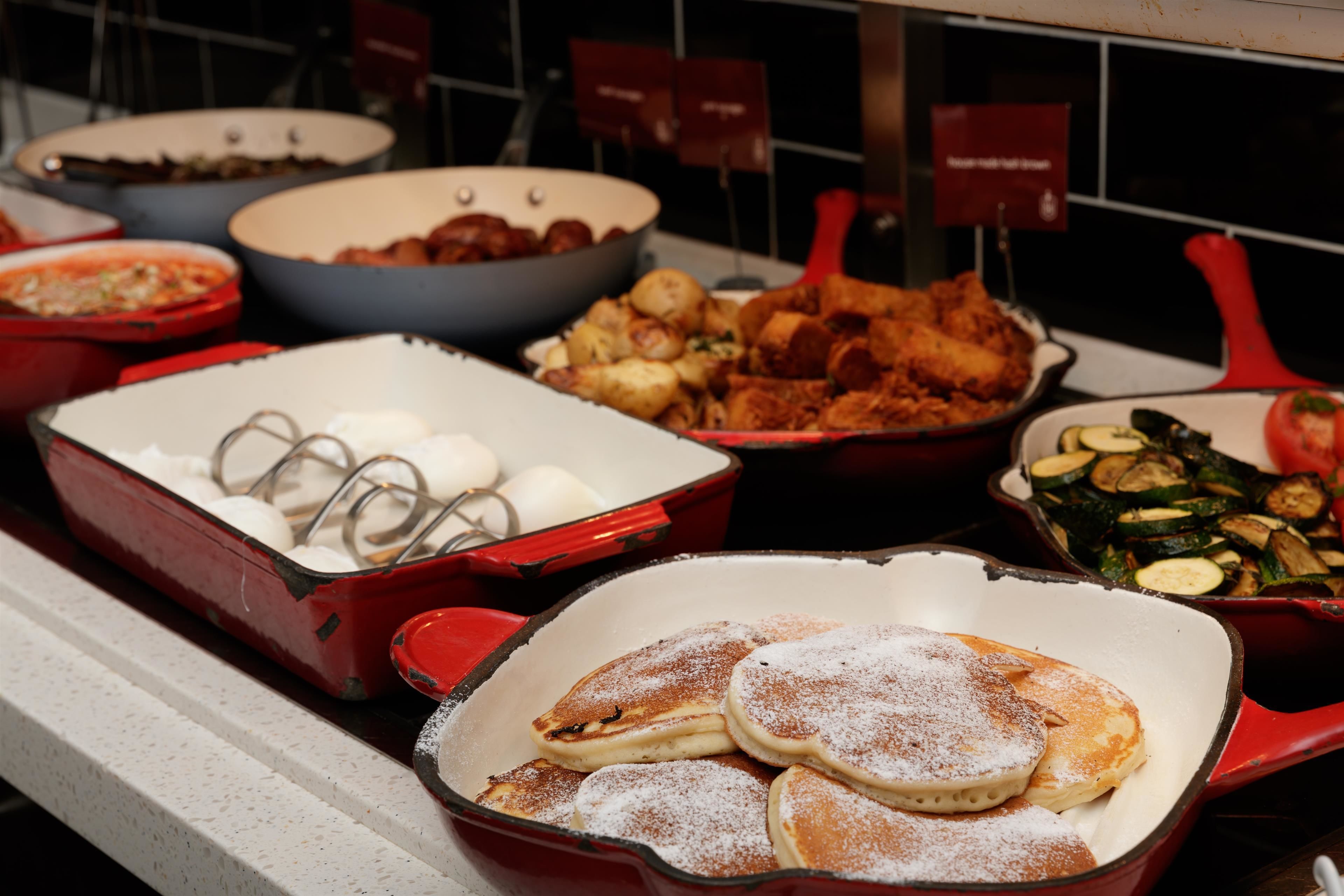 Een buffet met diverse gerechten, waaronder pannenkoeken, gefrituurde kip en groenten.