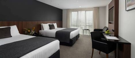 A hotel room with two beds, a desk, and a chair.