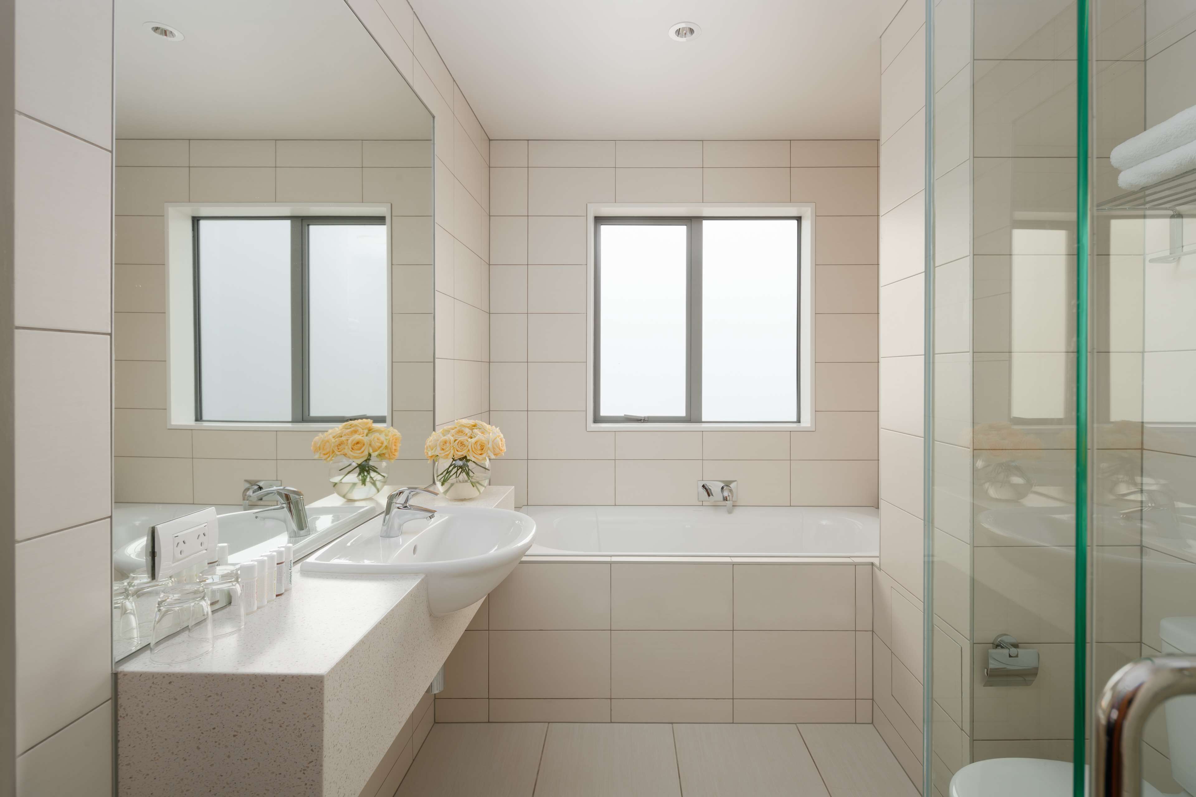 Ein modernes Badezimmer mit zwei Waschbecken, einer Badewanne und einer Duschkabine aus Glas.